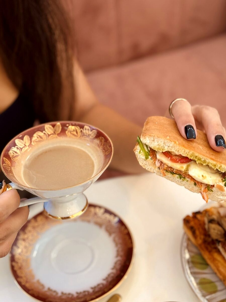 Cafea servită în ceașcă de porțelan, alături de un panini, pe masa din salonul Enza's Bakery